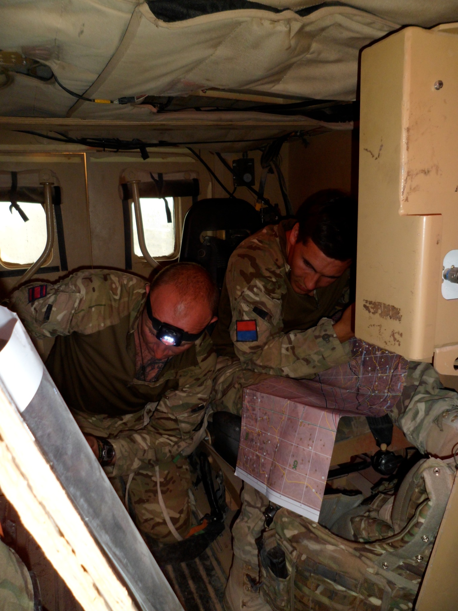Military personnel working together over a map inside a vehicle